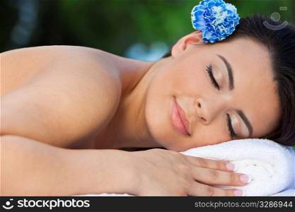 A beautiful brunette hispanic latina woman relaxing outside on a massage table at a health spa with a bue flower in her hair
