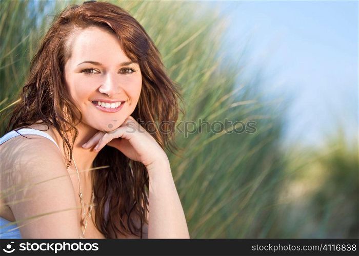 A beautiful brunette model sits amid tall grass illuminated by natural late evening golden sunshine
