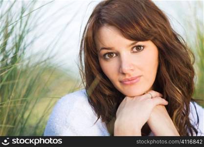 A beautiful brunette model sitting amid tall grass illuminated by natural sunlight