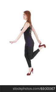 A beautiful brunette woman in a black outfit and high heels standingon one leg, looking serious, isolated for white background