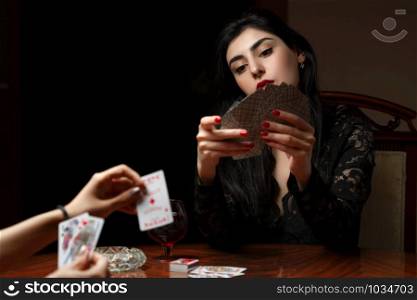 a beautiful brunette woman with scarlet lips in black clothes sits at a table and plays cards for undressing