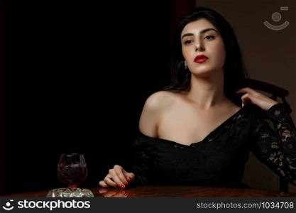 a beautiful brunette woman with scarlet lips in black clothes sits at a table and undresses after losing at cards