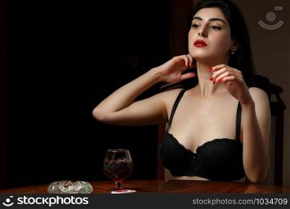 a beautiful brunette woman with scarlet lips in black lingerie sits at a table and plays cards for undressing