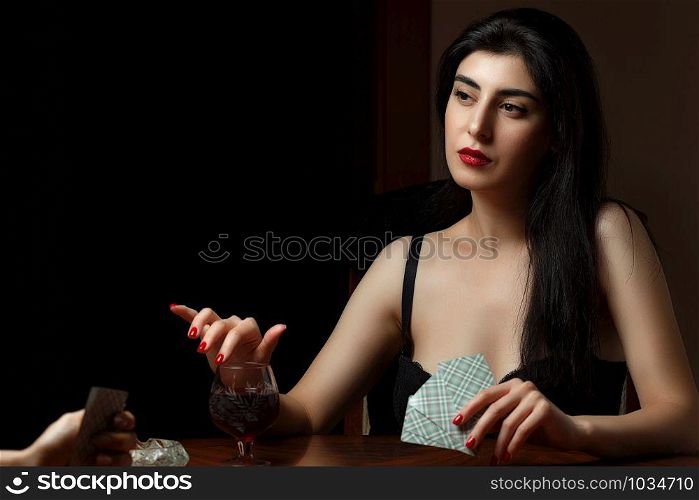 a beautiful brunette woman with scarlet lips in black lingerie sits at a table and plays cards for undressing