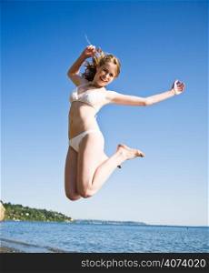 A beautiful caucasian girl jumping in joy on the beach during summer