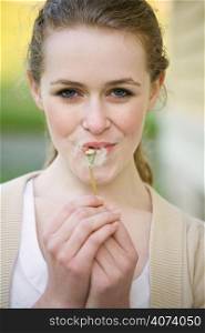 A beautiful caucasian teenage girl outdoor in summer blowing dandellion