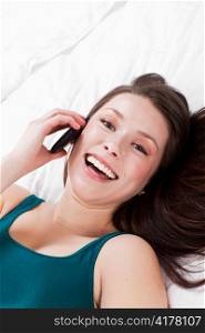 A beautiful caucasian woman lying down on the bed talking on the phone