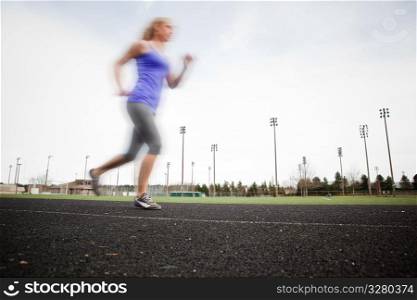 A beautiful caucasian woman running in a sport field (intentional blurred, with sharp focus on the running track)