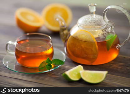 A beautiful composition of black tea and the addition of citrus. Glass teapot and cup of black tea with orange, lemon, lime mint on a wooden table