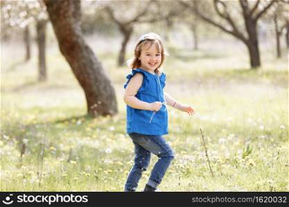 A beautiful cute little girl laughs and has fun in a blue blouse with a chamomile flower in a spring garden. A beautiful cute little girl laughs and has fun in a blue blouse with a chamomile flower in a spring garden.