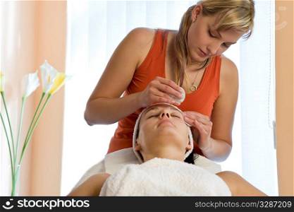A beautiful dark haired woman recieves a facial treatment from a young blonde beautician