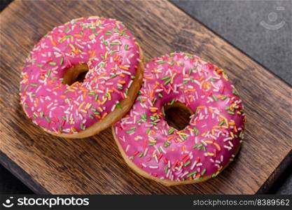 A beautiful doughnut with pink glaze and colored sprinkle on a dark concrete background. Sweets to the dinner table. A beautiful doughnut with pink glaze and colored sprinkle on a dark concrete background