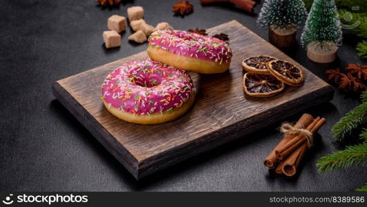 A beautiful doughnut with pink glaze and colored sprinkle on a dark concrete background. Sweets to the christmas table. A beautiful doughnut with pink glaze and colored sprinkle on a christmas table