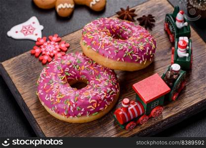 A beautiful doughnut with pink glaze and colored sprinkle on a dark concrete background. Sweets to the christmas table. A beautiful doughnut with pink glaze and colored sprinkle on a christmas table