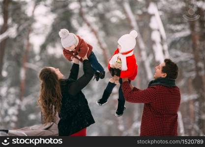 A beautiful family enjoying in the winter snowy forest. Mother, father, daughter and baby son enjoying day outdoors. Holidays, christmas, happiness together, childhood in love.
