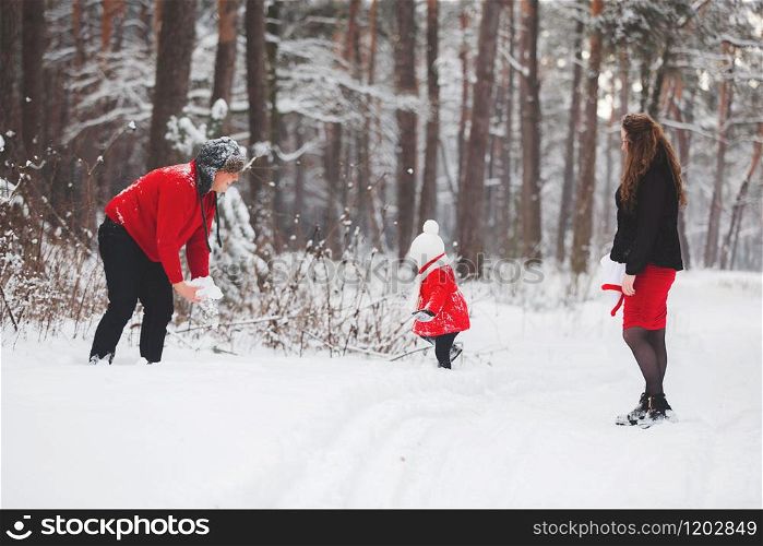 A beautiful family have fun in the winter snowy forest. Mother, father and daugther in red clothes enjoying day outdoors. Holidays, christmas, happiness together, childhood in love.