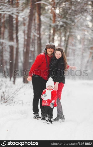 A beautiful family have fun in the winter snowy forest. Mother, father and daugther in red clothes enjoying day outdoors. Holidays, christmas, happiness together, childhood in love.