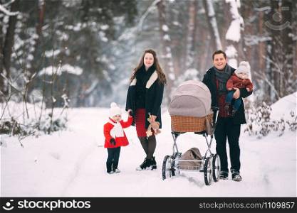 A beautiful family with retro pram walks through the winter snowy forest. Mother, father, daughter and baby son enjoying day outdoors. Holidays, christmas, happiness together, childhood in love.