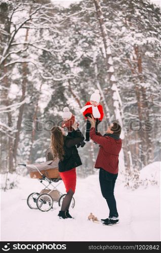 A beautiful family with retro pram walks through the winter snowy forest. Mother, father, daughter and baby son enjoying day outdoors. Holidays, christmas, happiness together, childhood in love.