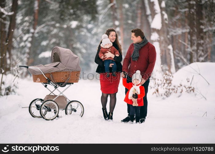 A beautiful family with retro pram walks through the winter snowy forest. Mother, father, daughter and baby son enjoying day outdoors. Holidays, christmas, happiness together, childhood in love.