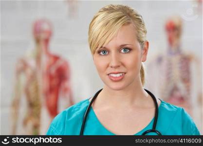 A beautiful female doctor in surgical scrubs shot in a hospital with human anatomy posters out of focus behind her.