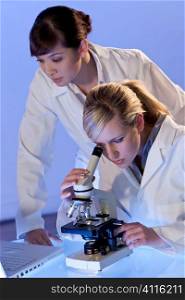 A beautiful female medical or scientific researcher using her microscope with her oriental colleague out of focus behind her.
