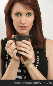 A beautiful female with vivid green eyes drinking tea or coffee.