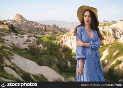 a beautiful girl in a dress and hat is enjoying the mountain landscape in Cappadocia
