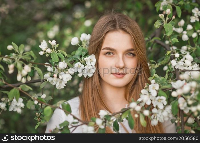 A beautiful girl in a long beige raincoat near a blooming cherry bush.. Portrait of a red-haired beauty in the spring nature 2952.