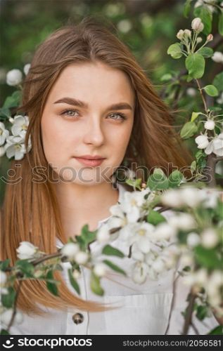 A beautiful girl in a long beige raincoat near a blooming cherry bush.. Portrait of a red-haired beauty in the spring nature 2953.