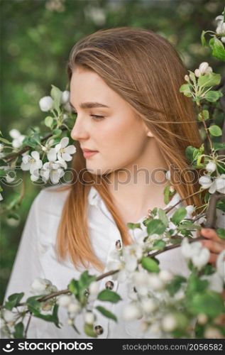 A beautiful girl in a long beige raincoat near a blooming cherry bush.. Portrait of a red-haired beauty in the spring nature 2954.
