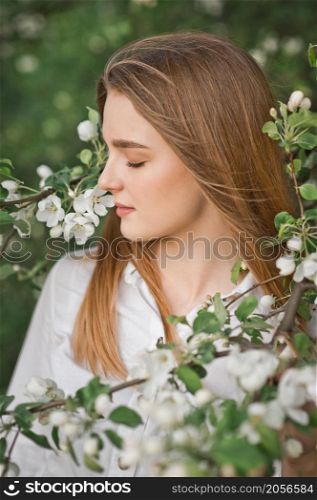 A beautiful girl in a long beige raincoat near a blooming cherry bush.. Portrait of a red-haired beauty in the spring nature 2955.