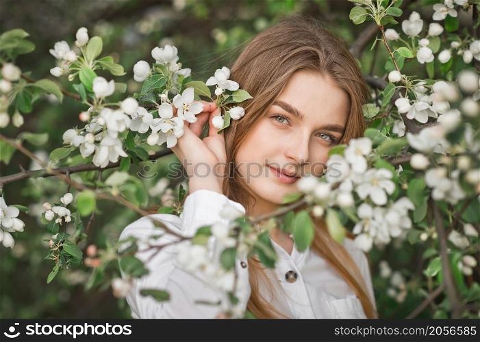 A beautiful girl in a long beige raincoat near a blooming cherry bush.. Portrait of a red-haired beauty in the spring nature 2956.