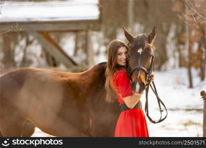 A beautiful girl in a red dress hugs a horse in the rays of the setting sun