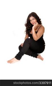 A beautiful girl in black jeans and bare feet with long black curly hairsitting on the floor for white background.