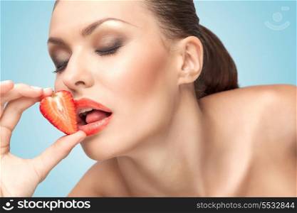 A beautiful girl licking a red juicy strawberry with a temptating tongue.