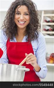 A beautiful girl or young woman looking happy wearing red apron &amp; cooking in her kitchen at home