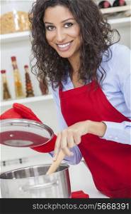 A beautiful girl or young woman looking happy wearing red apron &amp; cooking in her kitchen at home