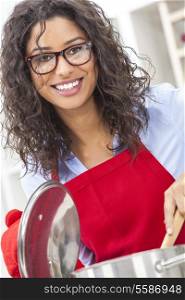A beautiful girl or young woman looking happy wearing red apron, glasses &amp; cooking in her kitchen at home