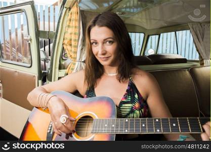 A beautiful girl plays the guitar while sitting in the back of her classic combi van.