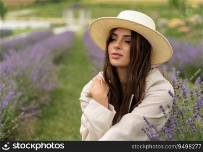 a beautiful girl with long hair and wearing a hat poses outdoors in a field of lavender