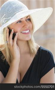 A beautiful girl young female woman with blond haor &amp; blue eyes talking on her cell phone wearing white sun hat and little black dress
