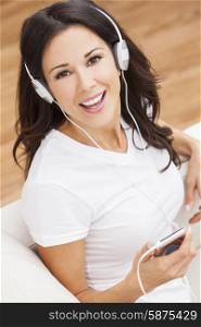 A beautiful happy girl or young woman sitting down listening to music on mp3 player and headphones