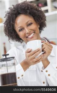 A beautiful happy mixed race African American girl or young woman drinking cafetiere coffee in her kitchen at home