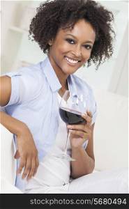 A beautiful happy mixed race African American girl or young woman drinking red wine at home on a white sofa