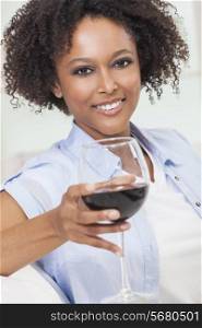 A beautiful happy mixed race African American girl or young woman drinking red wine at home on a white sofa