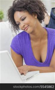 A beautiful happy mixed race African American girl or young woman laying down on sofa using a laptop computer