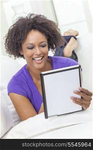 A beautiful happy mixed race African American girl or young woman laying down on sofa using a tablet computer