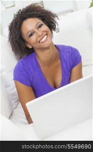 A beautiful happy mixed race African American girl or young woman laying down on sofa using a laptop computer