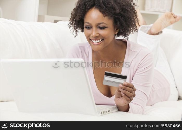 A beautiful happy mixed race African American girl or young woman laying down on sofa using a laptop computer shopping on line using her credit card